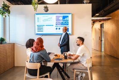 Senior Multiracial Male Manager Presenting Strategic Dashboard to Diverse Colleagues in Modern Office