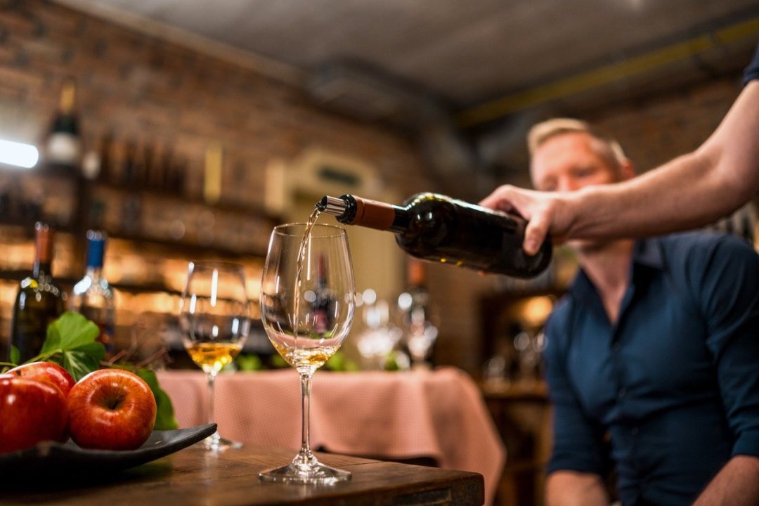 Sommelier pouring wine for guests at a table in a wine cellar
